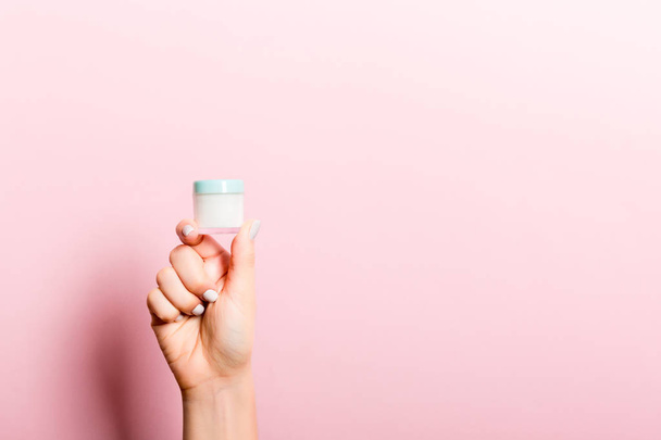 Female hand holding cream bottle of lotion isolated. Girl give jar cosmetic products on pink background - 写真・画像