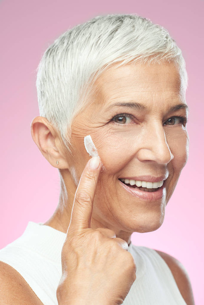 Gorgeous smiling Caucasian senior woman trying out new anti age cream. Beauty photography. - 写真・画像