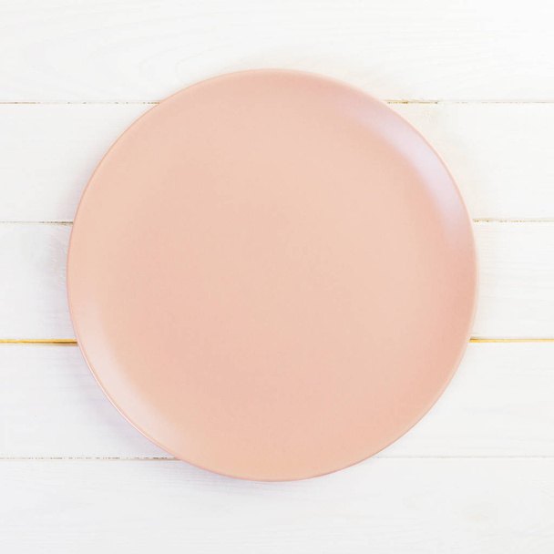 Ürítse ki a rózsaszín vagy korall kerek lemezt a fa asztal hátterére. Felülnézet, sablon a tervhez - Fotó, kép