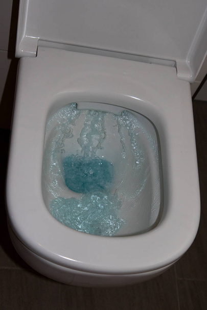 общий вид туалетного ключа с большим количеством поднимающейся синей воды в ванной комнате, сфотографированной крупным планом и разноцветной
 - Фото, изображение