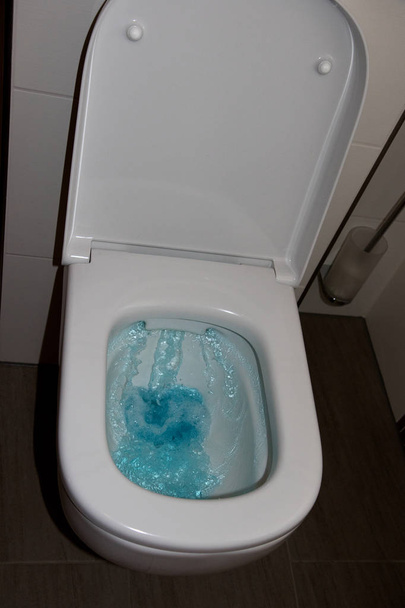 クローズアップとマルチカラーで撮影されたバスルームに上昇青い水の多くを持つトイレの総ビュー - 写真・画像