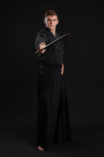 Кендо гуру, одягнений в традиційне джапан кімоно, практикує бойове мистецтво з шинайським бамбуковим мечем на чорному тлі студії.. - Фото, зображення