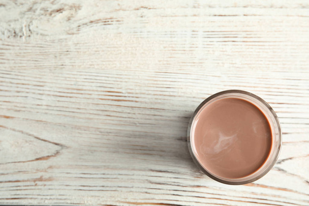 Glass of tasty chocolate milk on wooden background, top view with space for text. Dairy drink - Fotó, kép