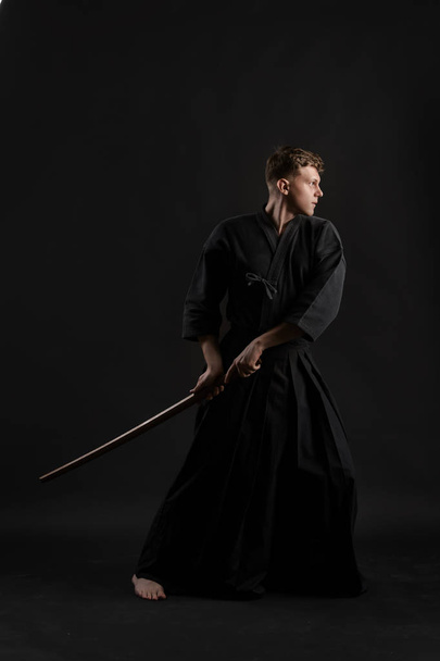 Kendo guru wearing in a traditional japanese kimono is practicing martial art with the shinai bamboo sword against a black studio background. - Foto, imagen