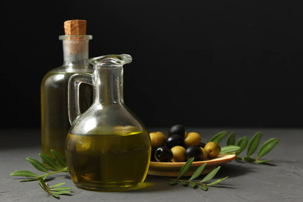 Aceite de oliva, hojas verdes y aceitunas sobre la mesa. - Foto, imagen