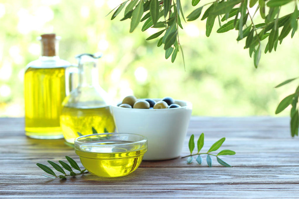 Aceite de oliva, hojas verdes y aceitunas sobre la mesa. - Foto, imagen