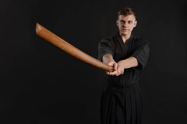 Kendo guru wearing in a traditional japanese kimono is practicing martial art with the shinai bamboo sword against a black studio background. - Photo, Image