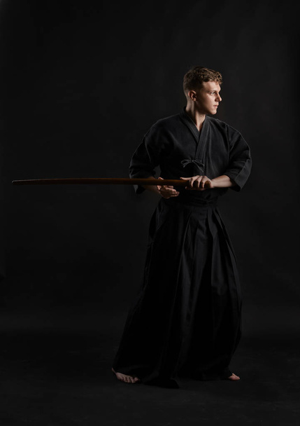 Geleneksel Japon kimonosu giymiş Kendo gurusu Shinai bambu kılıcıyla siyah bir stüdyoda dövüş sanatları eğitimi alıyor.. - Fotoğraf, Görsel