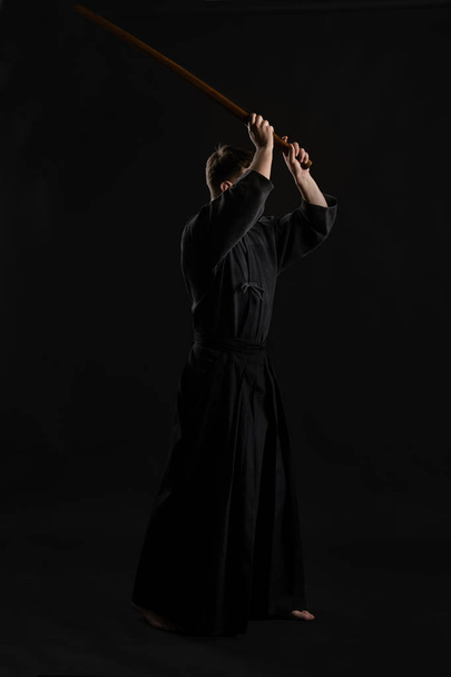 Kendo goeroe draagt in een traditionele Japanse kimono is het beoefenen van krijgskunst met de shinai bamboe zwaard tegen een zwarte studio achtergrond. - Foto, afbeelding
