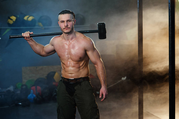 Strong muscular man with hammer on the shoulder. - Фото, изображение