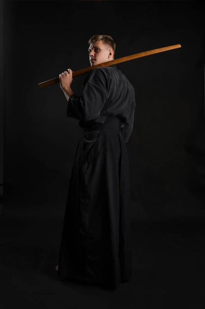 Kendo guru usando un kimono tradicional japonés está practicando el arte marcial con la espada de bambú shinai sobre un fondo de estudio negro.. - Foto, Imagen