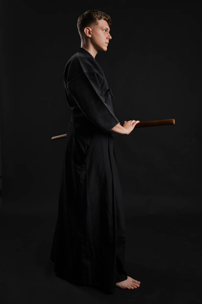 Kendo guru w tradycyjnym japońskim kimono ćwiczy sztukę walki mieczem bambusowym Shinai na czarnym tle studia. - Zdjęcie, obraz