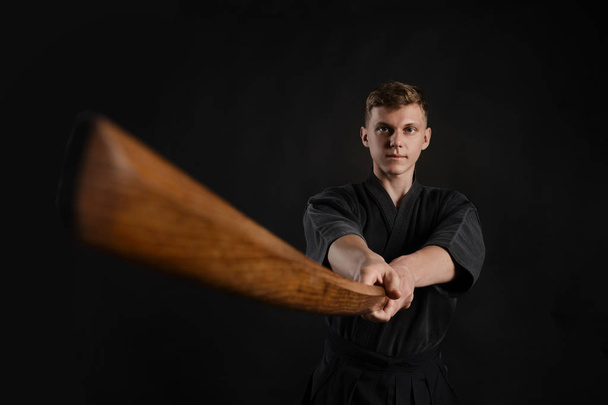 Kendo guru wearing in a traditional japanese kimono is practicing martial art with the shinai bamboo sword against a black studio background. - Photo, Image