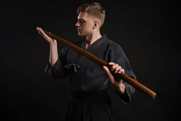 Kendo guru φορώντας ένα παραδοσιακό ιαπωνικό κιμονό ασκεί πολεμικές τέχνες με το σπαθί μπαμπού shinai σε μαύρο φόντο στούντιο. - Φωτογραφία, εικόνα