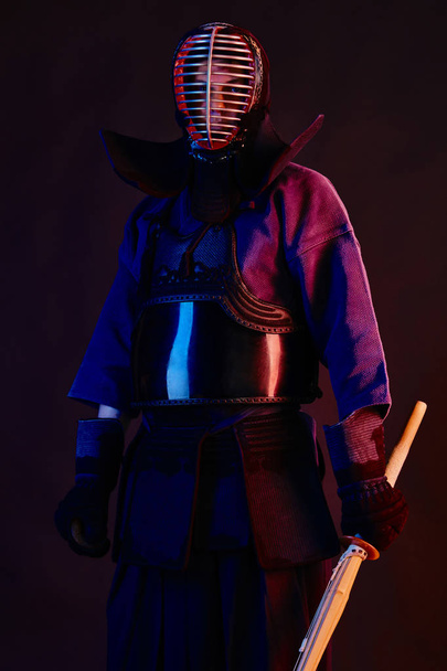 Close up shot, Kendo fighter wearing in an armor, traditional kimono, helmet practicing martial art with shinai bamboo sword, black background. - Foto, afbeelding