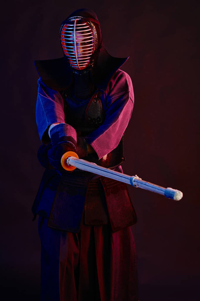 Close up shot, Kendo fighter wearing in an armor, traditional kimono, helmet practicing martial art with shinai bamboo sword, black background. - Zdjęcie, obraz
