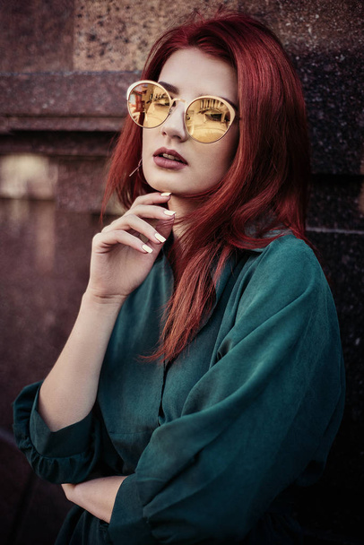 Nuori muodikas nainen romanttinen vihreä mekko ja punaiset hiukset, poseeraa lähellä taloja kadulla
. - Valokuva, kuva