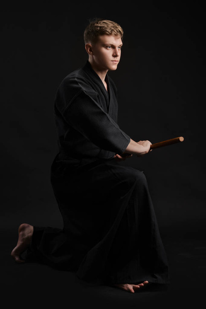 Kendo-Guru im traditionellen japanischen Kimono praktiziert Kampfkunst mit dem Shinai-Bambusschwert vor schwarzem Studiohintergrund. - Foto, Bild