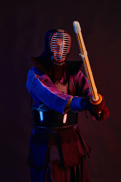Close up shot, Kendo fighter wearing in an armor, traditional kimono, helmet practicing martial art with shinai bamboo sword, black background. - Φωτογραφία, εικόνα