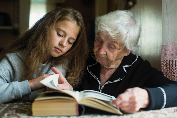 An elderly woman is reading a book to her beloved granddaughter. - Photo, Image