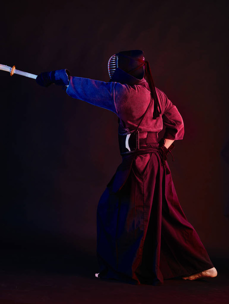 Primo piano, combattente Kendo in armatura, kimono tradizionale, casco praticare arte marziale con spada di bambù shinai, sfondo nero
. - Foto, immagini