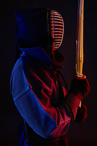 Close up shot, Kendo fighter wearing in an armor, traditional kimono, helmet practicing martial art with shinai bamboo sword, black background. - Foto, imagen