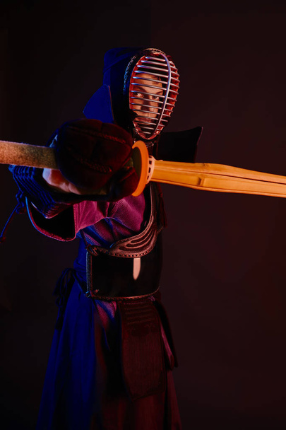 Primer plano, luchador Kendo con armadura, kimono tradicional, casco practicando arte marcial con espada de bambú shinai, fondo negro
. - Foto, imagen