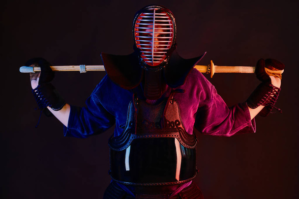 Close up shot, Kendo fighter wearing in an armor, traditional kimono, helmet practicing martial art with shinai bamboo sword, black background. - 写真・画像