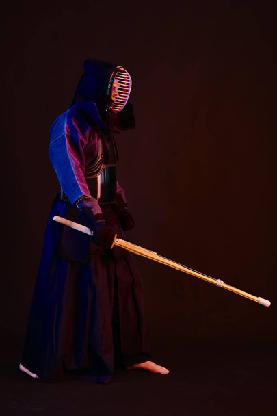 Strzał z bliska, myśliwiec Kendo w zbroi, tradycyjne kimono, kask ćwiczący sztukę walki z shinai bambusowym mieczem, czarne tło. - Zdjęcie, obraz