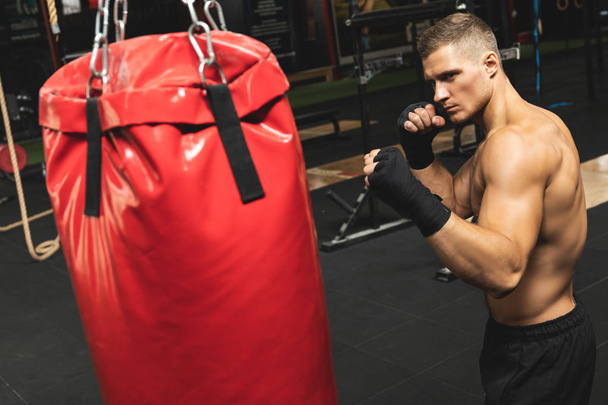 Strong young mma fighter and red punching bag - 写真・画像