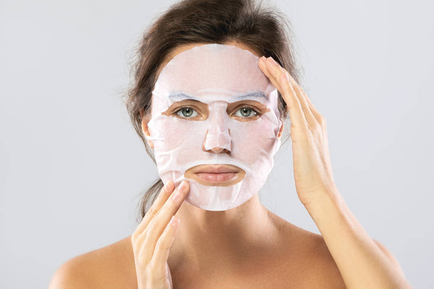 Woman with a sheet moisturizing mask on her face isolated on gra - Foto, Bild