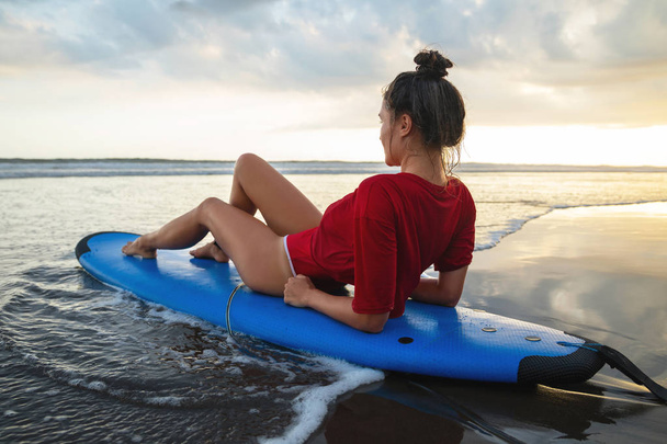 Woman sitting on surfboard on the beach after her surfing sessio - Fotoğraf, Görsel
