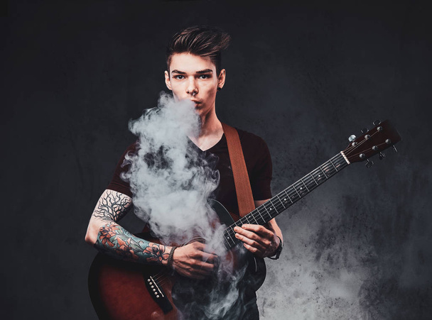 Cara atraente está tocando guitarra acústica e fumando
 - Foto, Imagem