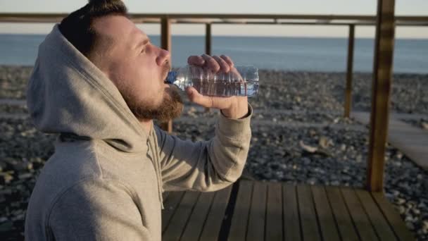 Hombre adulto se relaja en la orilla del mar, beber agua y respirar aire fresco
 - Metraje, vídeo