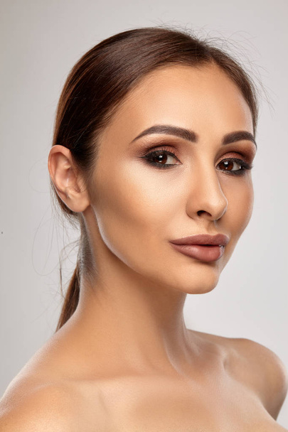 Close up portrait of a brunette nude model girl with professional evening make-up and plump lips, posing on gray background. - Φωτογραφία, εικόνα
