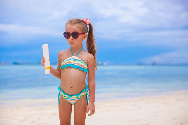 schattig meisje in zwembroek houdt zonnebrand lotion fles - Foto, afbeelding