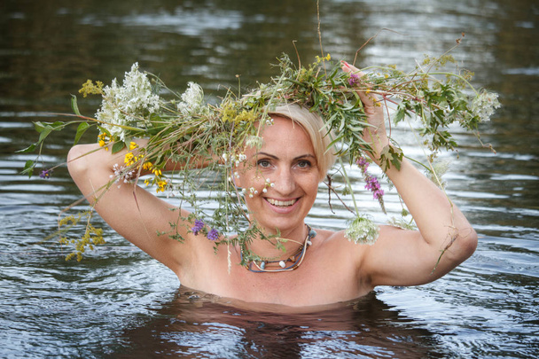 Mujer de mediana edad guirnalda rubia de flores silvestres en la cabeza nada en el lago, enfoque selectivo
 - Foto, Imagen