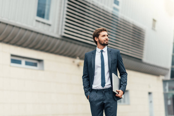Full length photo of a young business man unbuttoning the jacket of his suit while looking away from the camera - Foto, immagini