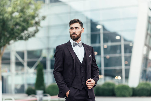 Young and successful. Handsome young man in full suit adjusting his jacket while standing outdoors - Photo, Image