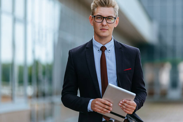 Happy smiling businessman with digital tablet. Portrait of a Male executive manager in trendy clothes with tablet PC in hand on background of office building. Modern technology concept - Foto, Bild