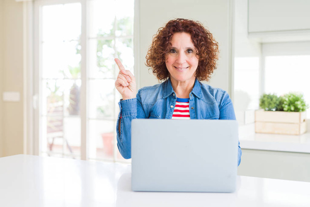 Starší žena pracující s počítačovým laptopem velmi šťastná ukazující rukou a prstem na stranu - Fotografie, Obrázek