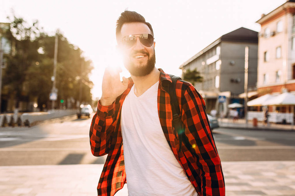 Stylish guy with a beard in wireless headphones walks around the city and listens to music - Foto, imagen
