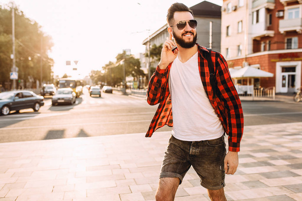 Stylish guy with a beard in wireless headphones walks around the city and listens to music. - Zdjęcie, obraz
