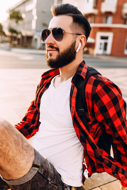 Stylish guy with a beard in wireless headphones listens to music - Zdjęcie, obraz