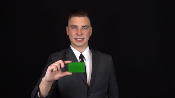 Een jonge zakenman in een pak houdt een bankkaart bij de hand. Geïsoleerde zwarte achtergrond. Chromakey groene kaart. 4k - Video