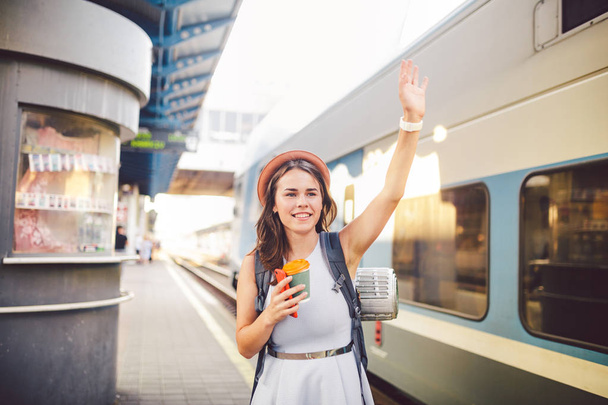 backpack traveler woman waving hand at train station platform summer holiday traveling concept. Female tourist greeting and enjoy on train, travel concept. Theme transportation and travel - Photo, Image