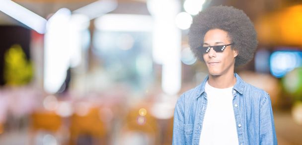 Молодий афроамериканець людина з афро волосся носіння Туг життя окуляри дивлячись у бік з посмішкою на обличчі, природний вираз. Сміється впевнено. - Фото, зображення