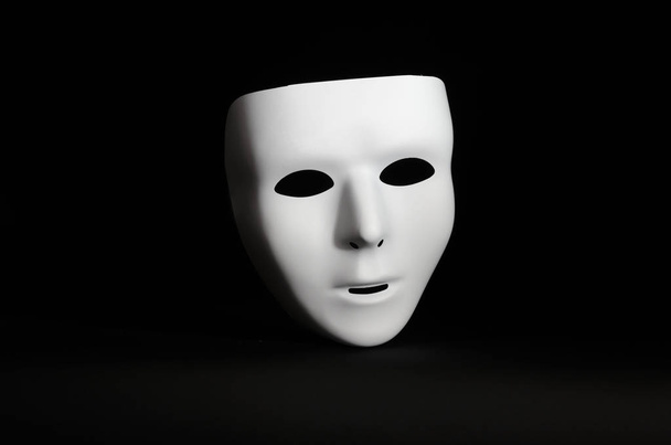 een blanco, emotieloze maskerade masker is gemarkeerd tegen een grimmige zwarte achtergrond  - Foto, afbeelding