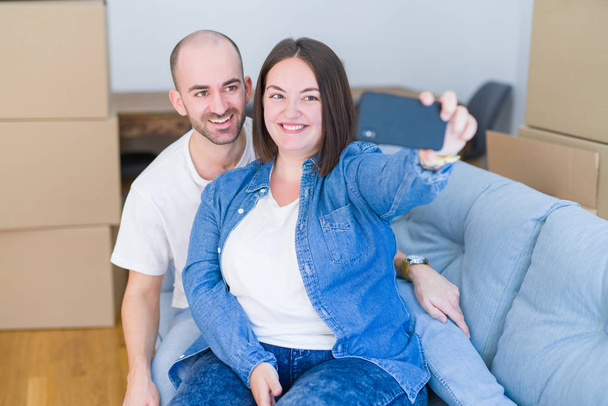 Молодая пара, сидящая на диване в новом доме, делает селфи фото, используя смартфон, улыбаясь счастливой, что переехала в новую квартиру.
 - Фото, изображение