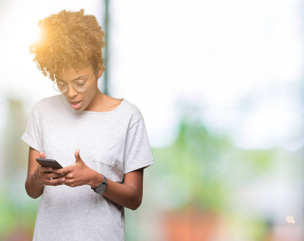 Νεαρός αφρικανική αμερικανική γυναίκα που χρησιμοποιούν smartphone πέρα από το απομονωμένο υπόβαθρο φοβάται το σοκ με πρόσωπο έκπληξη, φοβάται και ενθουσιασμένος με φόβο έκφραση - Φωτογραφία, εικόνα